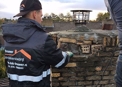 Een dakdekker van Dak-Brouwer uit Rotterdam en Den Haag renoveert een schoorsteen.